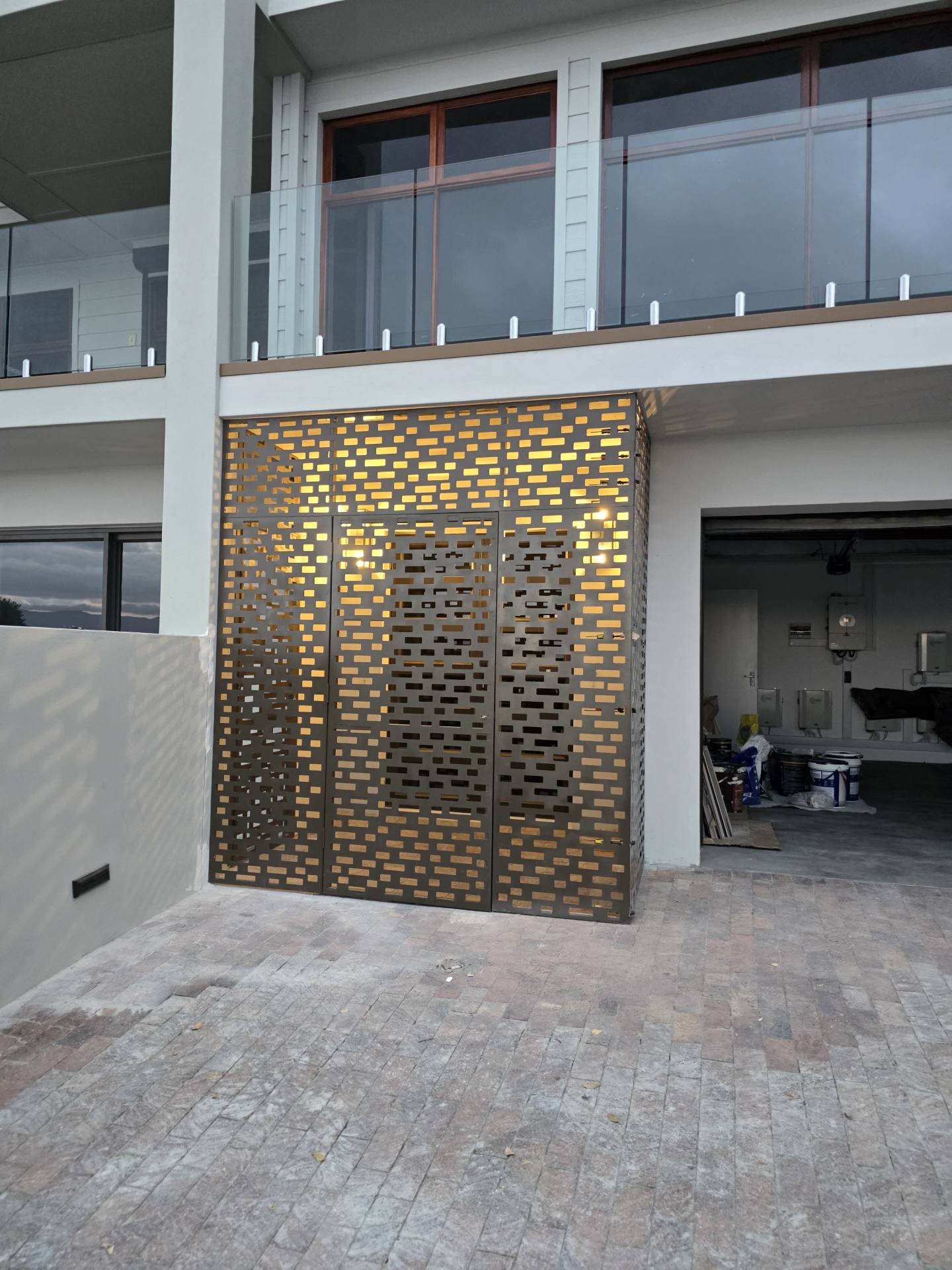 Laser-cut perforated steel entrance enclosure glowing at dusk, fabricated by Brandt Möbel Kreatif